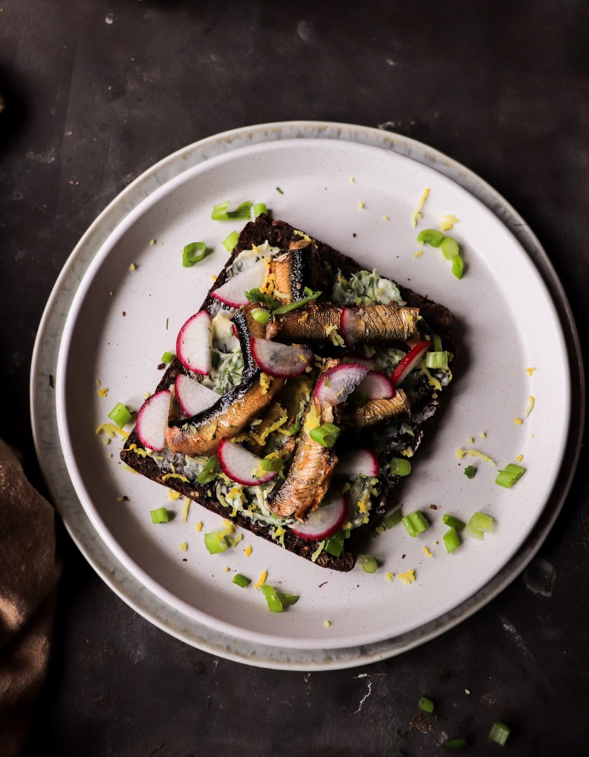 Baltic-inspired Smoked sprat rye toast with lemon butter and sliced radishes.