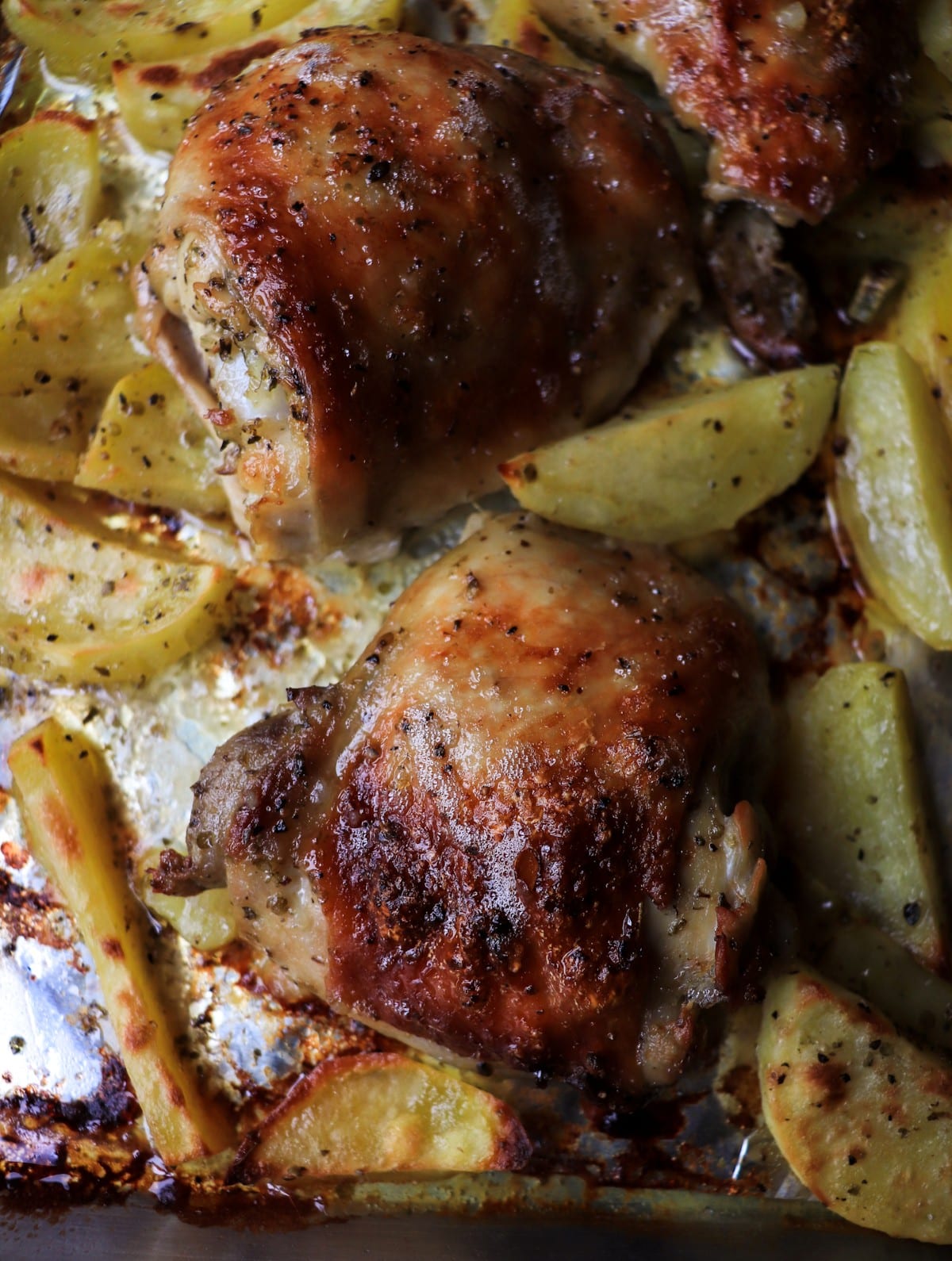 close up of Greek lemon oregano chicken thigh with crispy skin and roasted potatoes in lemon olive oil sauce