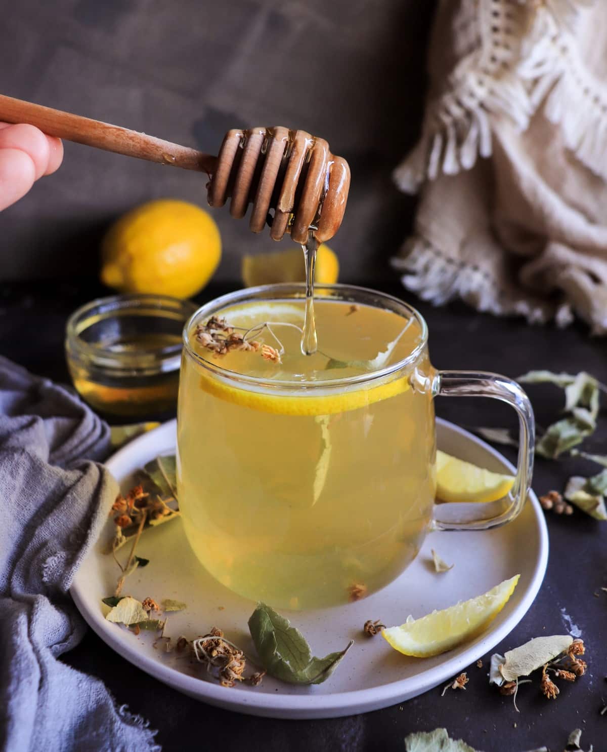 Linden tea with lemon and honey being drizzled into a glass mug with dried linden flowers