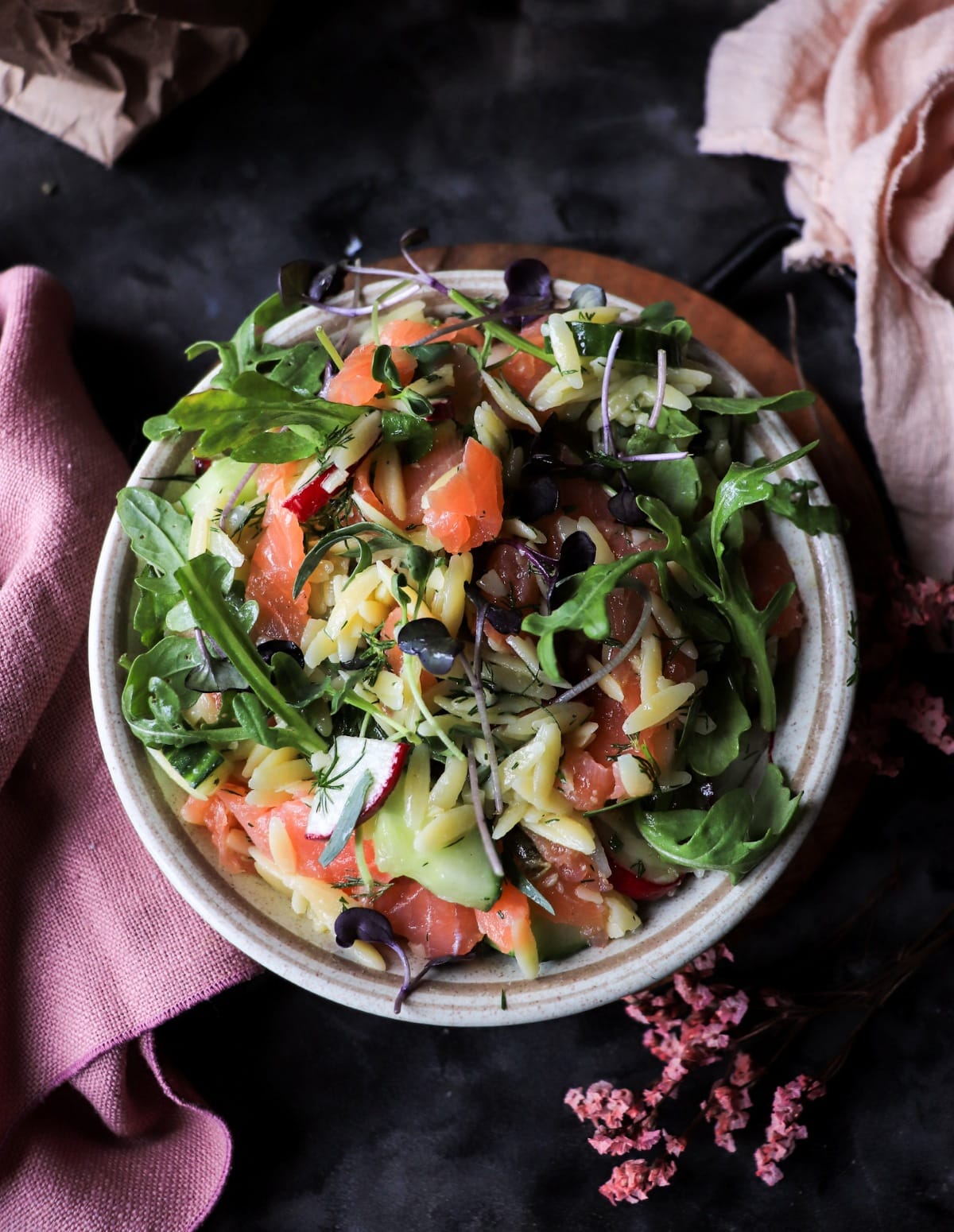 Smoked salmon salad with orzo pasta, fresh herbs, cucumber, and microgreens.