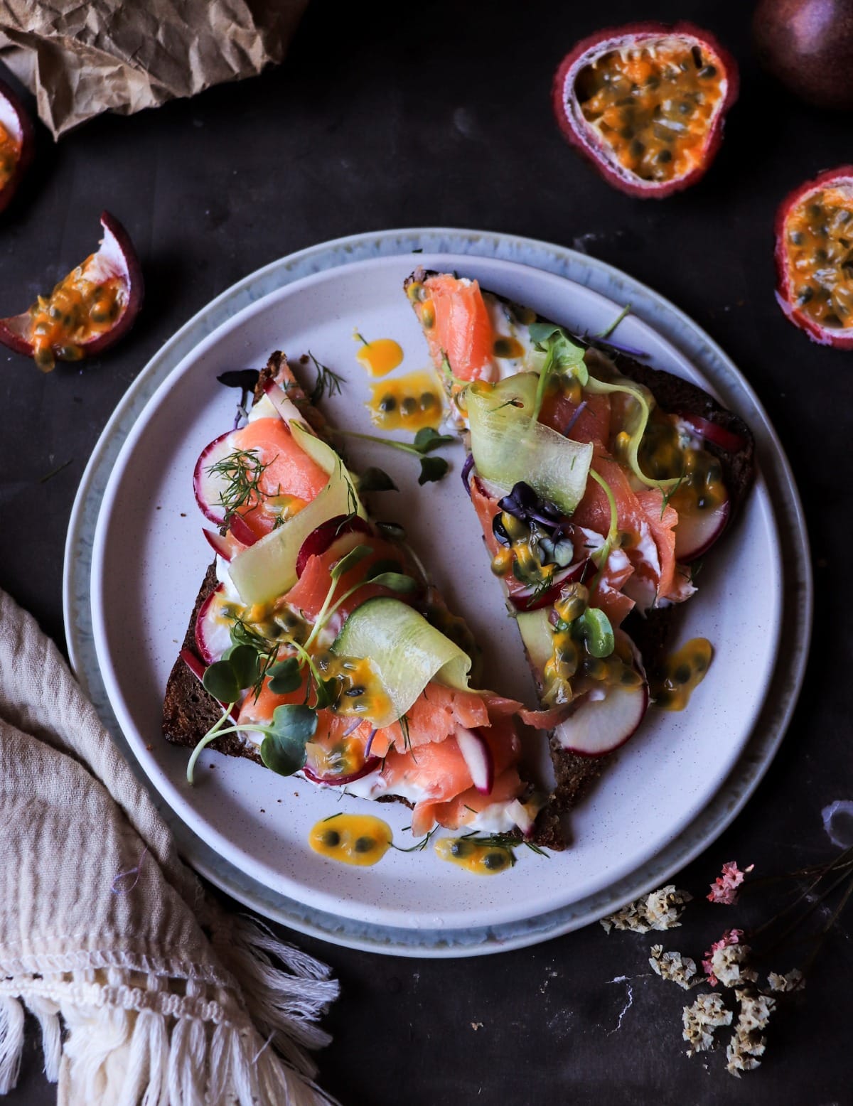 Rye toast with smoked salmon topped with cucumber ribbons, radishes, dill cream, and passion fruit