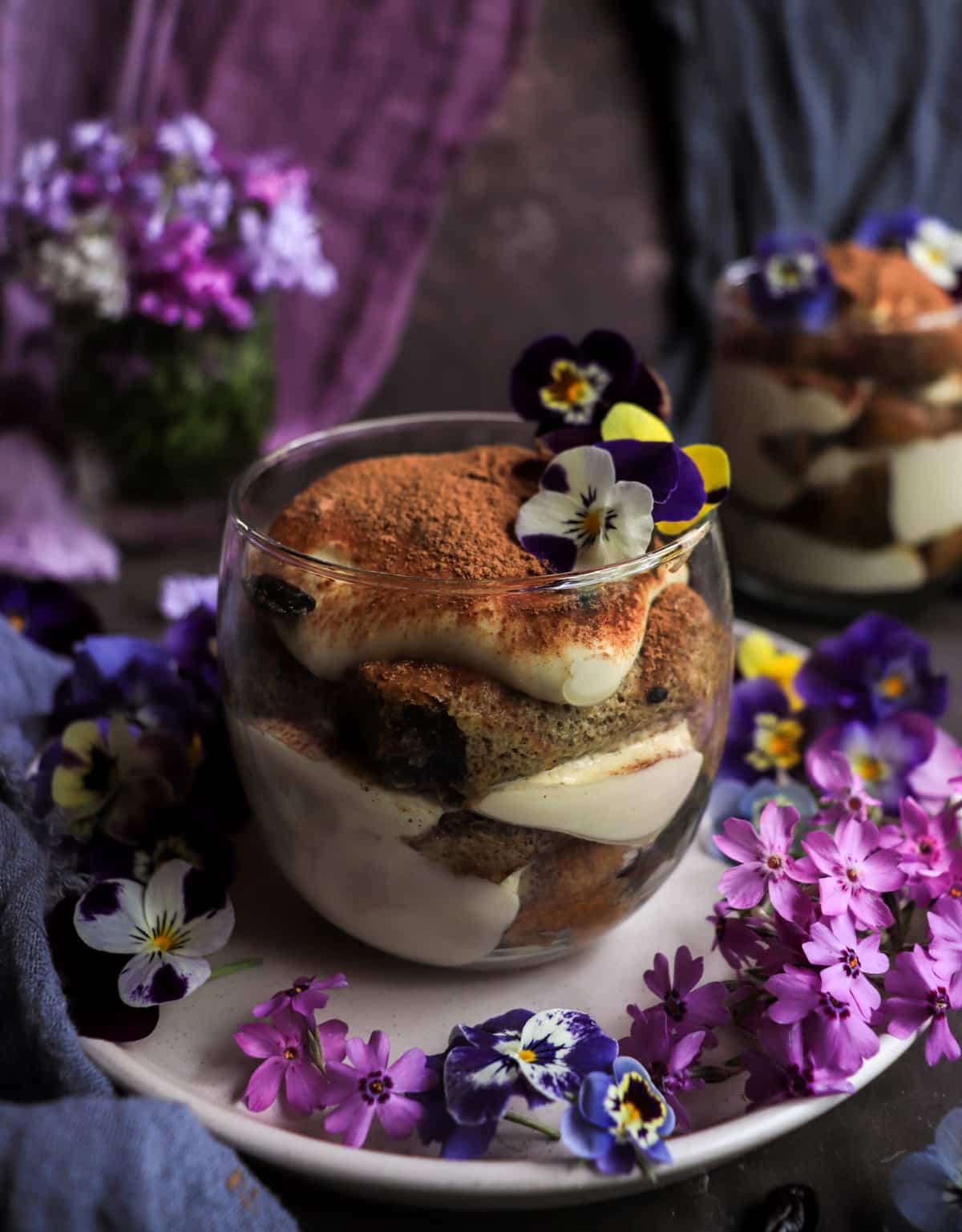Elegant violet tiramisu with edible flowers served in an individual dessert glass.