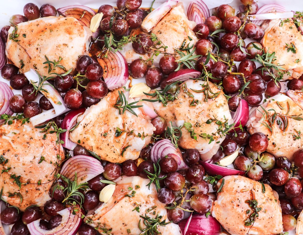 roasted chicken thighs with grapes, red onions, and herbs on a sheet pan before baking